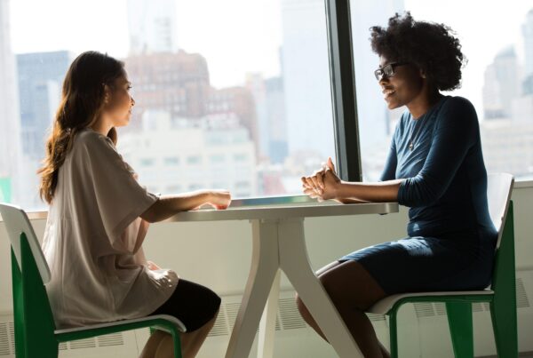 Dos mujeres sentadas en una mesa cara a cara teniendo una conversación.