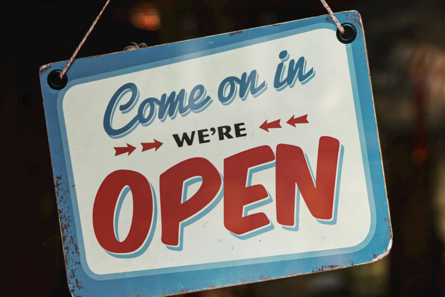 Cartel en ingĺes que dice "Come on in we're open" Colgando de un cristal, se entiende que de un negociio