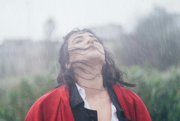 Mujer bajo la lluvia mojándose, mirando hacia arriba, parece en paz
