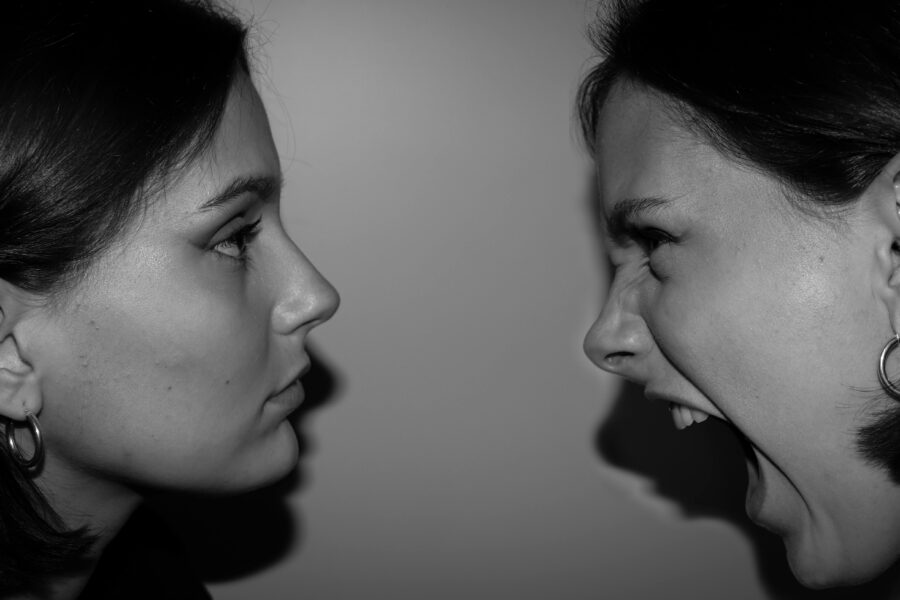 Dos mujeres enfrentadas, es posible que sean la misma mujer cara a cara, una esta neutra la otra está gritando visiblemente.