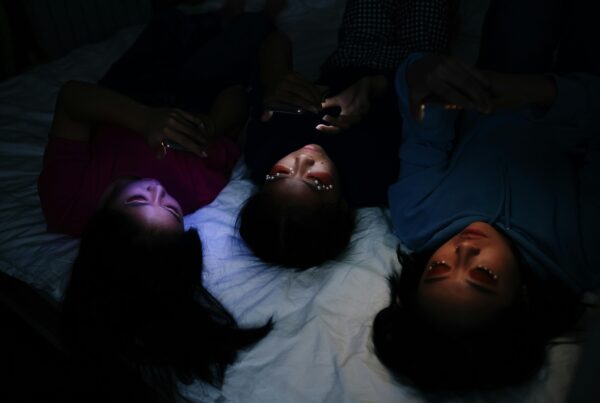 3 girls laying on bed in the dark looking at their phones